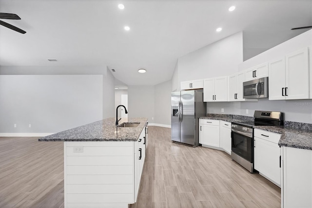 kitchen with stainless steel appliances, a kitchen island with sink, a sink, white cabinetry, and dark stone countertops