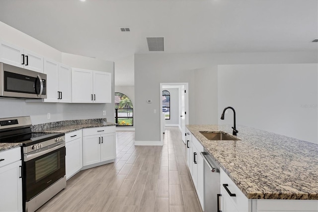 kitchen featuring white cabinets, an island with sink, appliances with stainless steel finishes, light stone countertops, and a sink