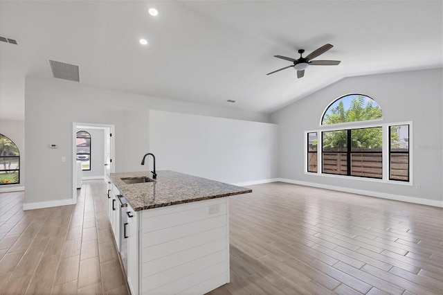 kitchen with visible vents, open floor plan, dark stone countertops, white cabinetry, and a sink