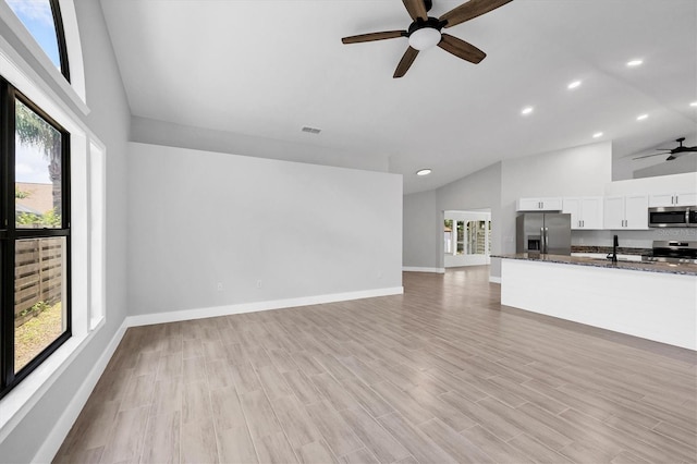 unfurnished living room with light wood-type flooring, a sink, a ceiling fan, and baseboards