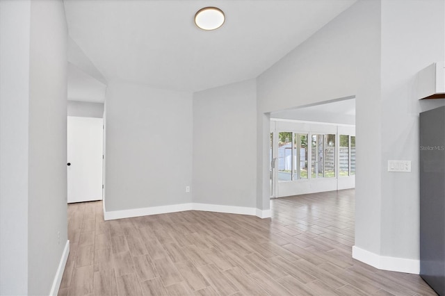 spare room featuring light wood-style floors, baseboards, and vaulted ceiling