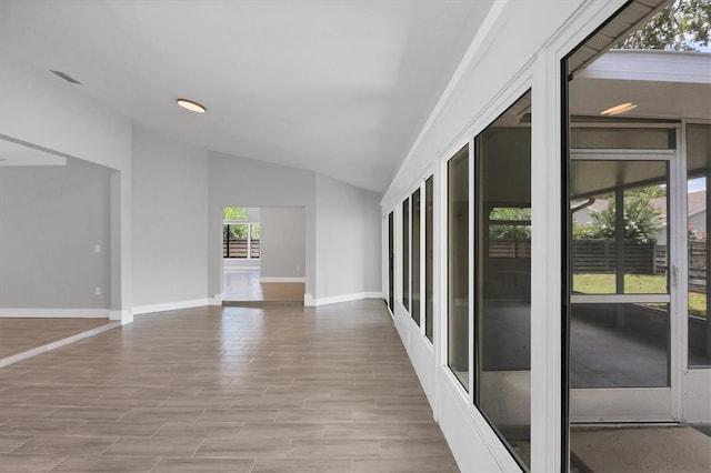 empty room with light wood-style floors, visible vents, baseboards, and vaulted ceiling