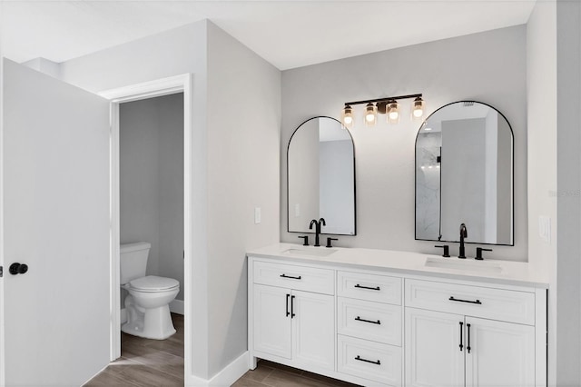 bathroom featuring toilet, double vanity, a sink, and wood finished floors