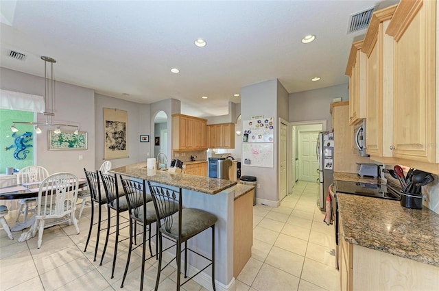 kitchen with light brown cabinetry, stainless steel appliances, light tile patterned floors, decorative light fixtures, and stone counters