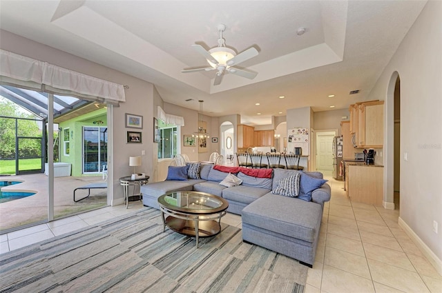 living room featuring ceiling fan, light tile patterned floors, and a tray ceiling