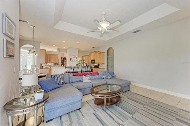 living room with a raised ceiling, ceiling fan, and light tile patterned flooring