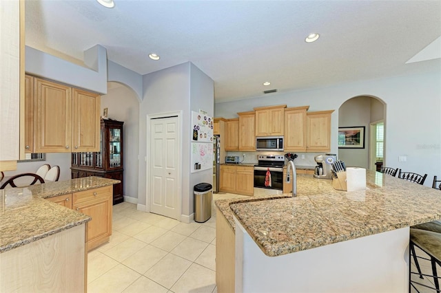 kitchen featuring a breakfast bar area, light stone countertops, light brown cabinetry, and stainless steel appliances