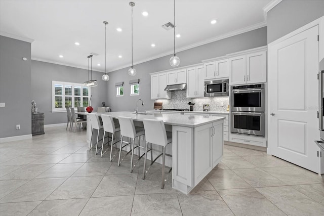 kitchen featuring white cabinets, crown molding, hanging light fixtures, an island with sink, and stainless steel appliances