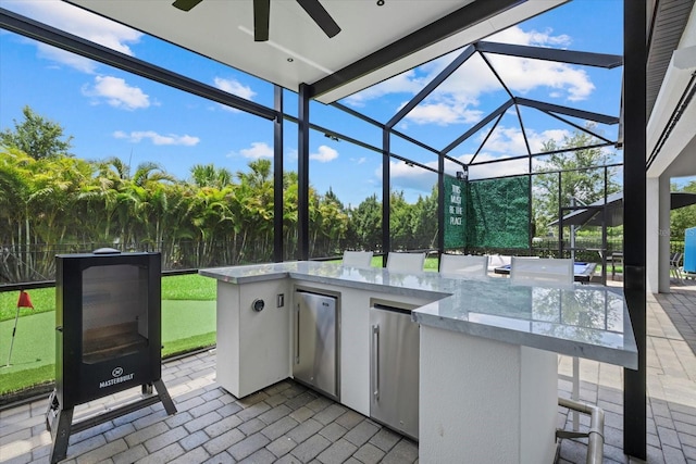 view of patio / terrace with a lanai, ceiling fan, exterior bar, and an outdoor kitchen