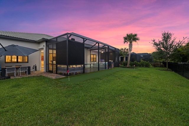 back house at dusk featuring a yard and glass enclosure