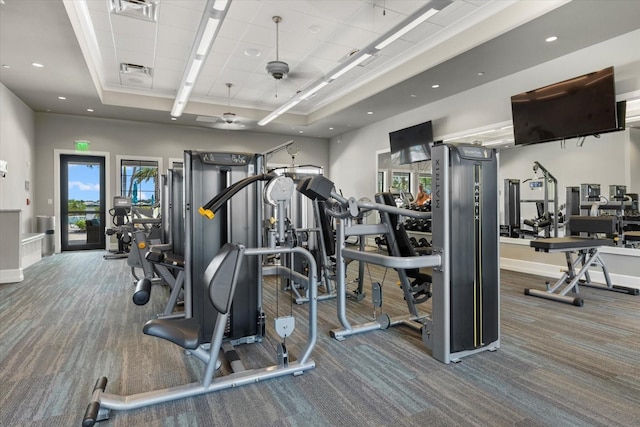 exercise room featuring a raised ceiling, ceiling fan, and carpet floors