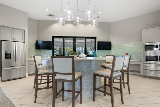 kitchen featuring a kitchen bar, appliances with stainless steel finishes, gray cabinetry, a kitchen island with sink, and decorative light fixtures