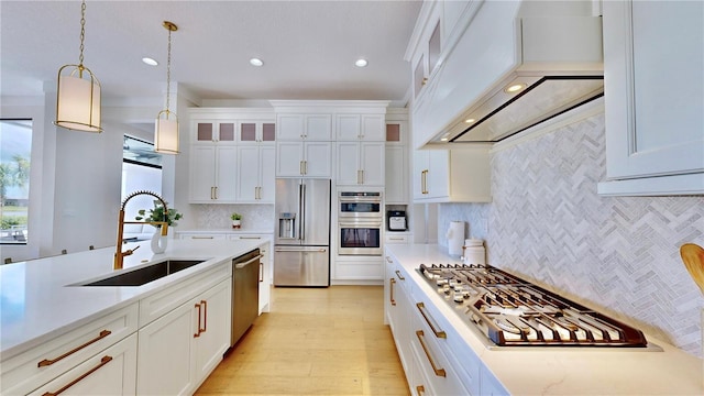 kitchen featuring white cabinetry, sink, decorative light fixtures, appliances with stainless steel finishes, and custom exhaust hood