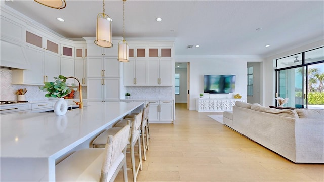 kitchen featuring hanging light fixtures, a kitchen breakfast bar, backsplash, a center island with sink, and white cabinets