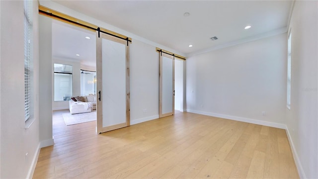 unfurnished room with a barn door, light hardwood / wood-style flooring, and crown molding