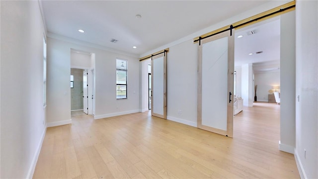 unfurnished room featuring a barn door, light wood-type flooring, and crown molding