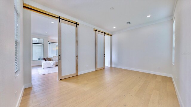 unfurnished room featuring a barn door, light wood-type flooring, and ornamental molding