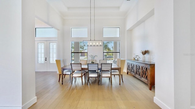 dining space featuring light hardwood / wood-style flooring, a high ceiling, french doors, and a notable chandelier