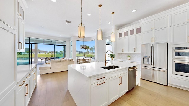 kitchen featuring stainless steel appliances, a kitchen island with sink, sink, white cabinetry, and hanging light fixtures