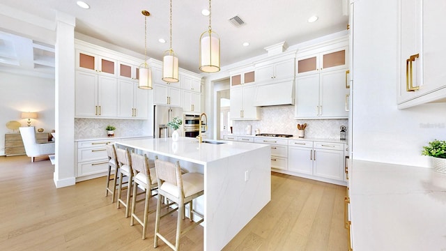 kitchen featuring a kitchen island with sink, hanging light fixtures, appliances with stainless steel finishes, white cabinetry, and a breakfast bar area