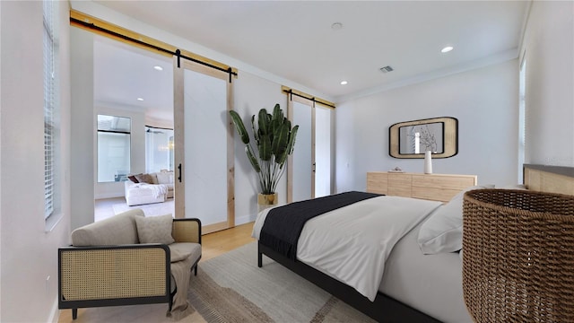 bedroom featuring a barn door, light wood-type flooring, and ornamental molding