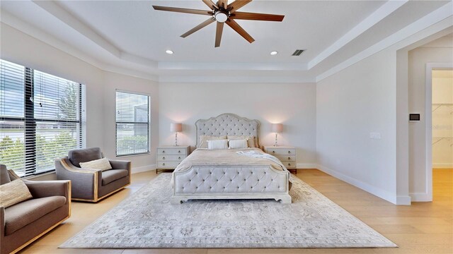 bedroom featuring light wood-type flooring, a raised ceiling, and ceiling fan