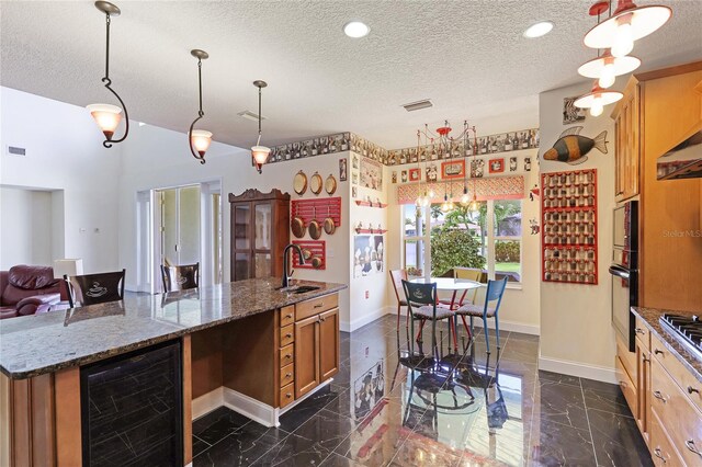 kitchen with sink, decorative light fixtures, beverage cooler, and stone counters