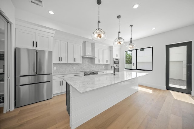 kitchen featuring white cabinets, wall chimney exhaust hood, light hardwood / wood-style floors, and appliances with stainless steel finishes