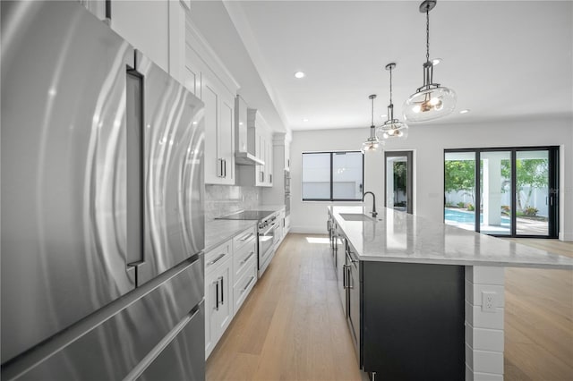 kitchen with a kitchen island with sink, white cabinets, hanging light fixtures, sink, and stainless steel appliances