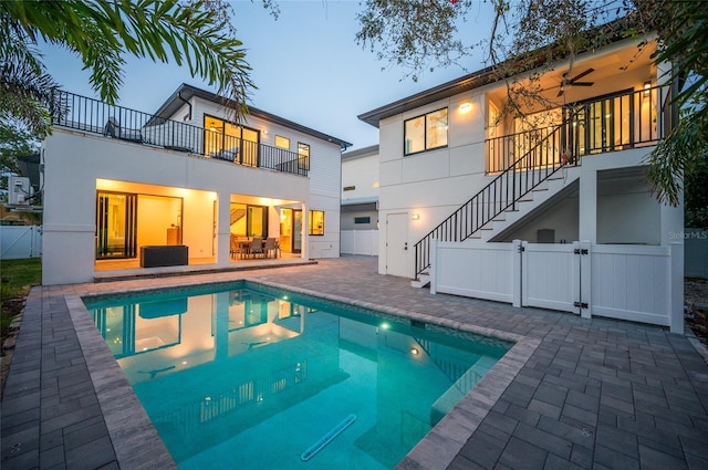 back house at dusk featuring a fenced in pool, a patio, a balcony, and ceiling fan