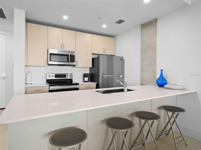 kitchen featuring light brown cabinets, a kitchen breakfast bar, sink, appliances with stainless steel finishes, and kitchen peninsula