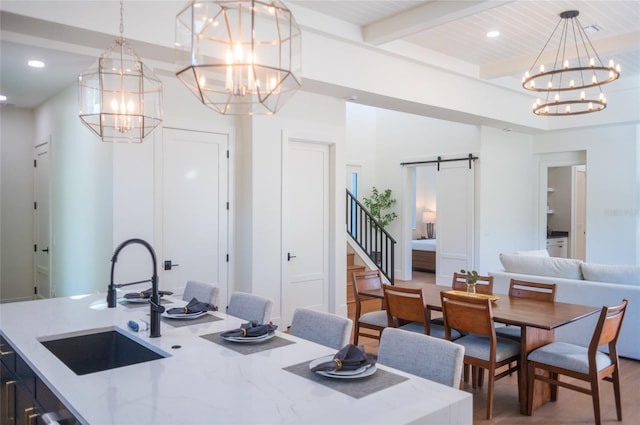 dining room featuring a barn door, sink, a notable chandelier, and beam ceiling