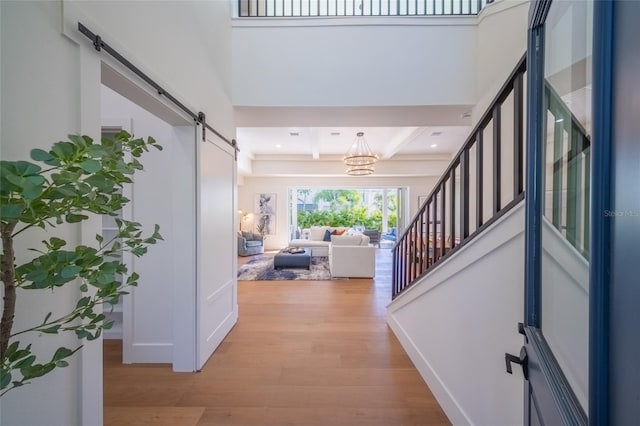 hall featuring beam ceiling, a barn door, a towering ceiling, and light hardwood / wood-style floors