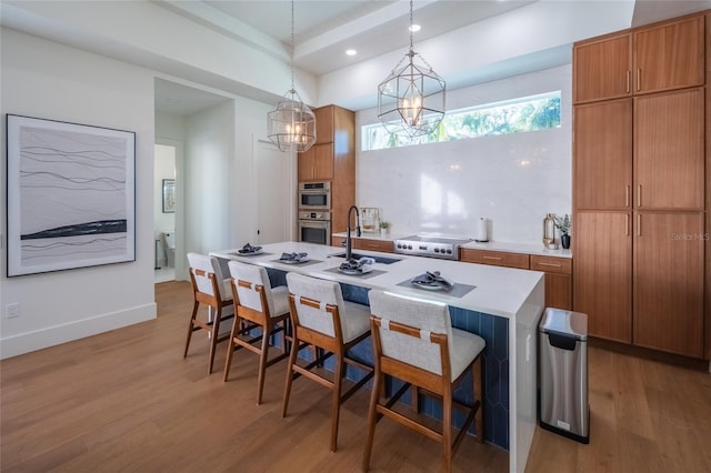 kitchen with a breakfast bar, sink, decorative light fixtures, a center island with sink, and light hardwood / wood-style floors