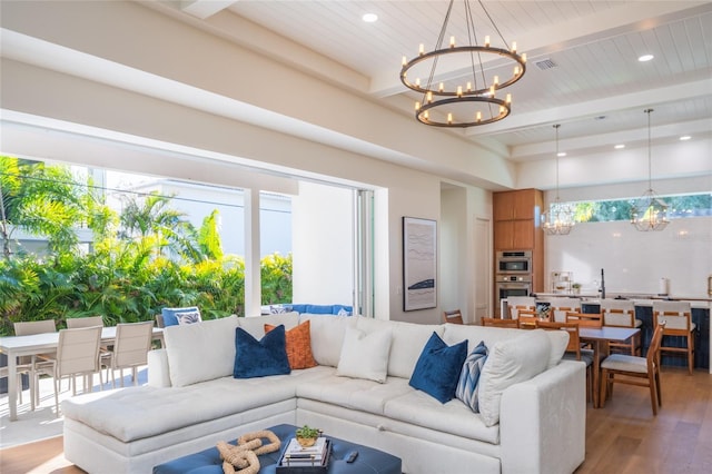 living room with an inviting chandelier, beam ceiling, and light wood-type flooring