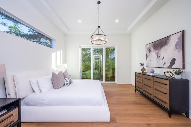 bedroom with light hardwood / wood-style flooring, a notable chandelier, and a tray ceiling