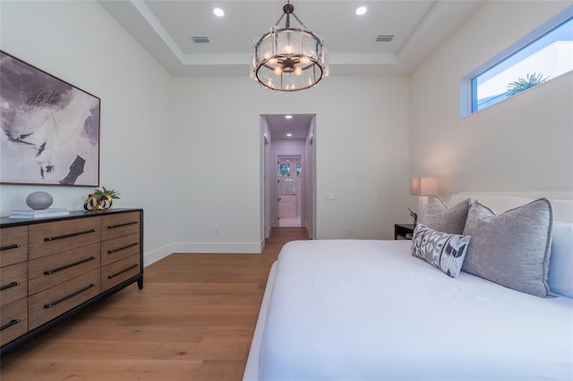 bedroom with an inviting chandelier, a raised ceiling, and light hardwood / wood-style floors