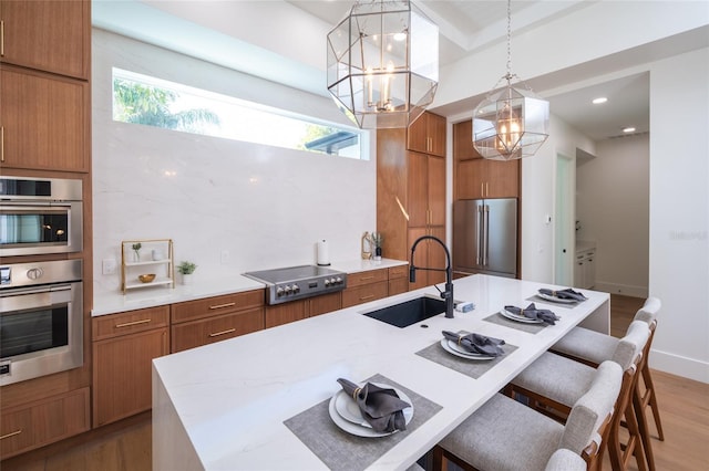 kitchen with sink, appliances with stainless steel finishes, wood-type flooring, an island with sink, and decorative light fixtures