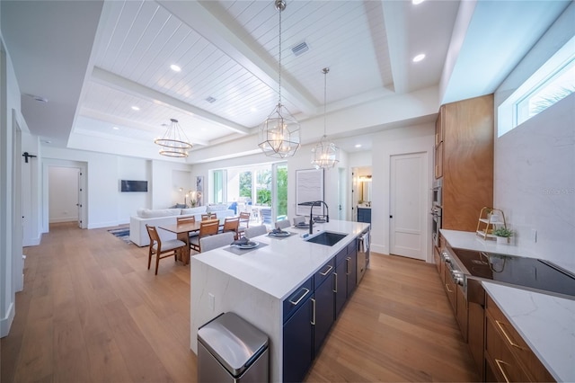 kitchen featuring an island with sink, wood-type flooring, sink, and decorative light fixtures