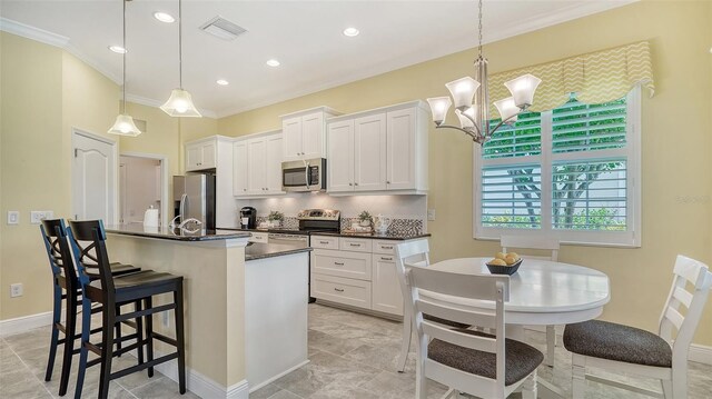 kitchen featuring white cabinetry, hanging light fixtures, stainless steel appliances, an island with sink, and a kitchen bar