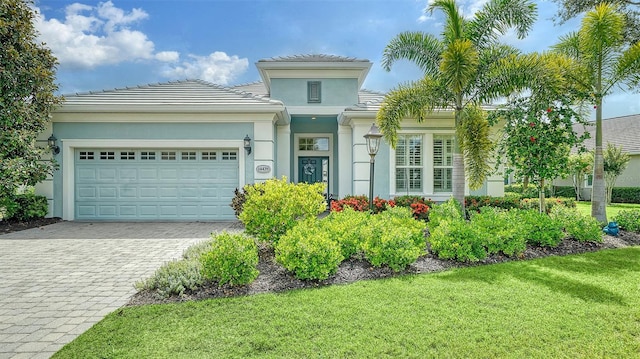 view of front of property featuring a garage, decorative driveway, a front lawn, and stucco siding