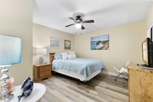 bedroom with light wood-style flooring, baseboards, ceiling fan, and a textured ceiling