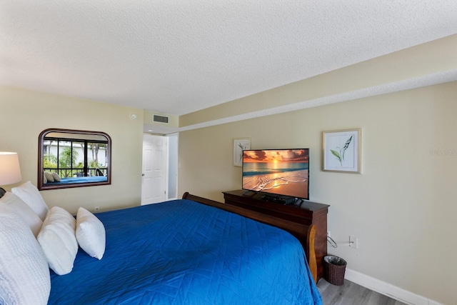 bedroom with baseboards, visible vents, a textured ceiling, and wood finished floors