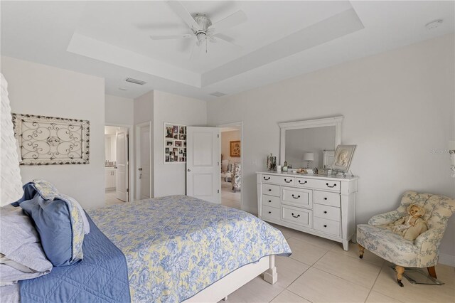 tiled bedroom with a tray ceiling, ceiling fan, and ensuite bath