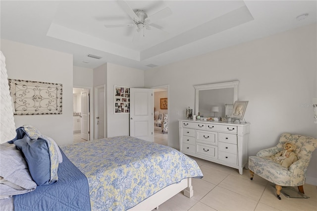 bedroom with light tile patterned flooring, ensuite bath, ceiling fan, and a tray ceiling