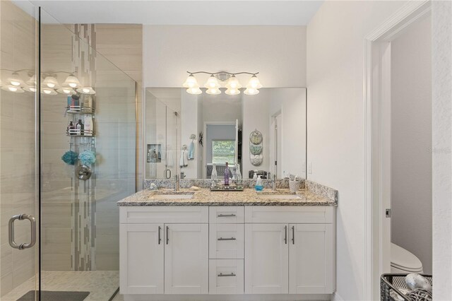 bathroom featuring dual sinks, vanity with extensive cabinet space, a shower with shower door, and toilet