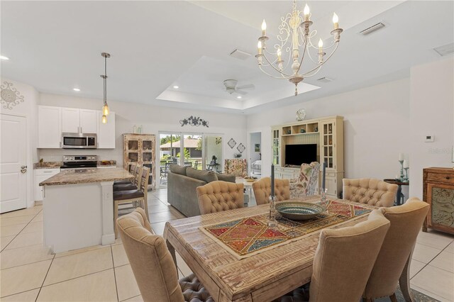 tiled dining space featuring ceiling fan with notable chandelier and a tray ceiling