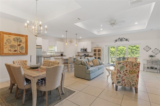 tiled dining room featuring sink, a tray ceiling, and ceiling fan with notable chandelier