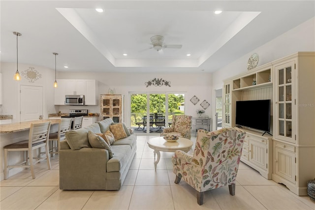 tiled living room with ceiling fan and a tray ceiling