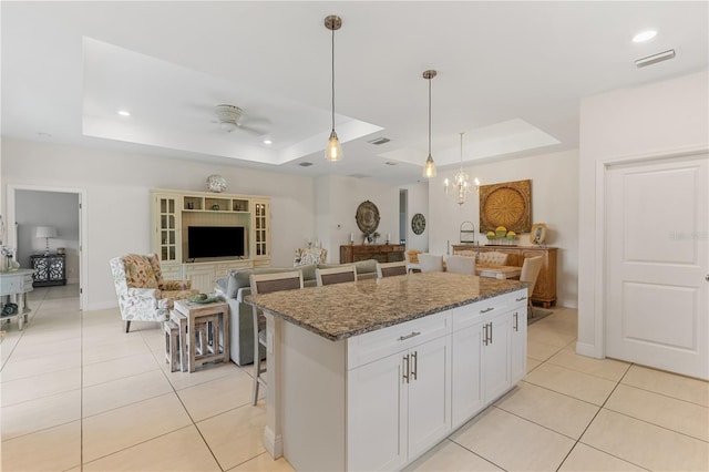 kitchen featuring ceiling fan, dark stone countertops, a raised ceiling, a kitchen island, and white cabinets